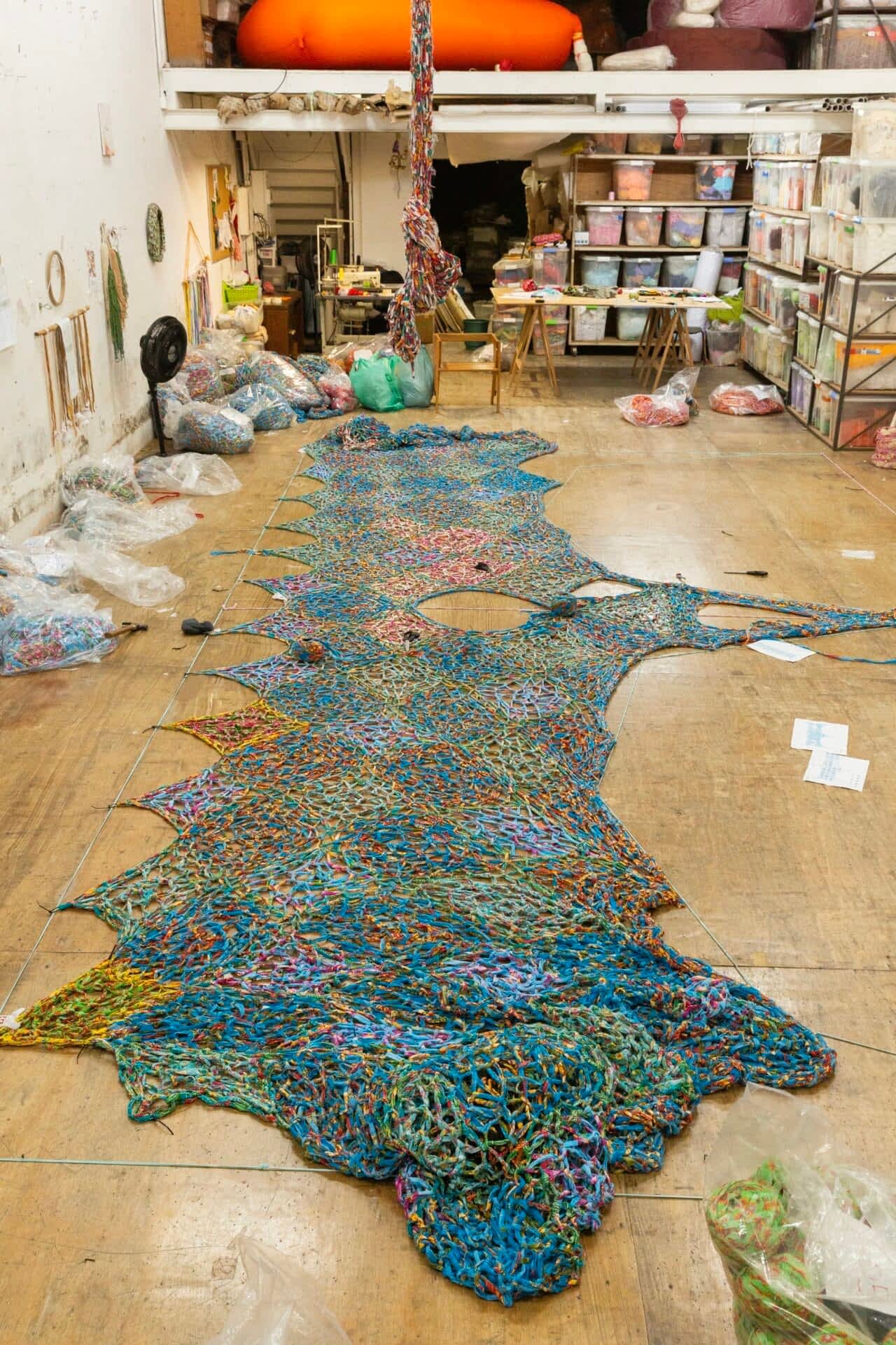 a large crocheted installation spread out on the floor of the artist's studio