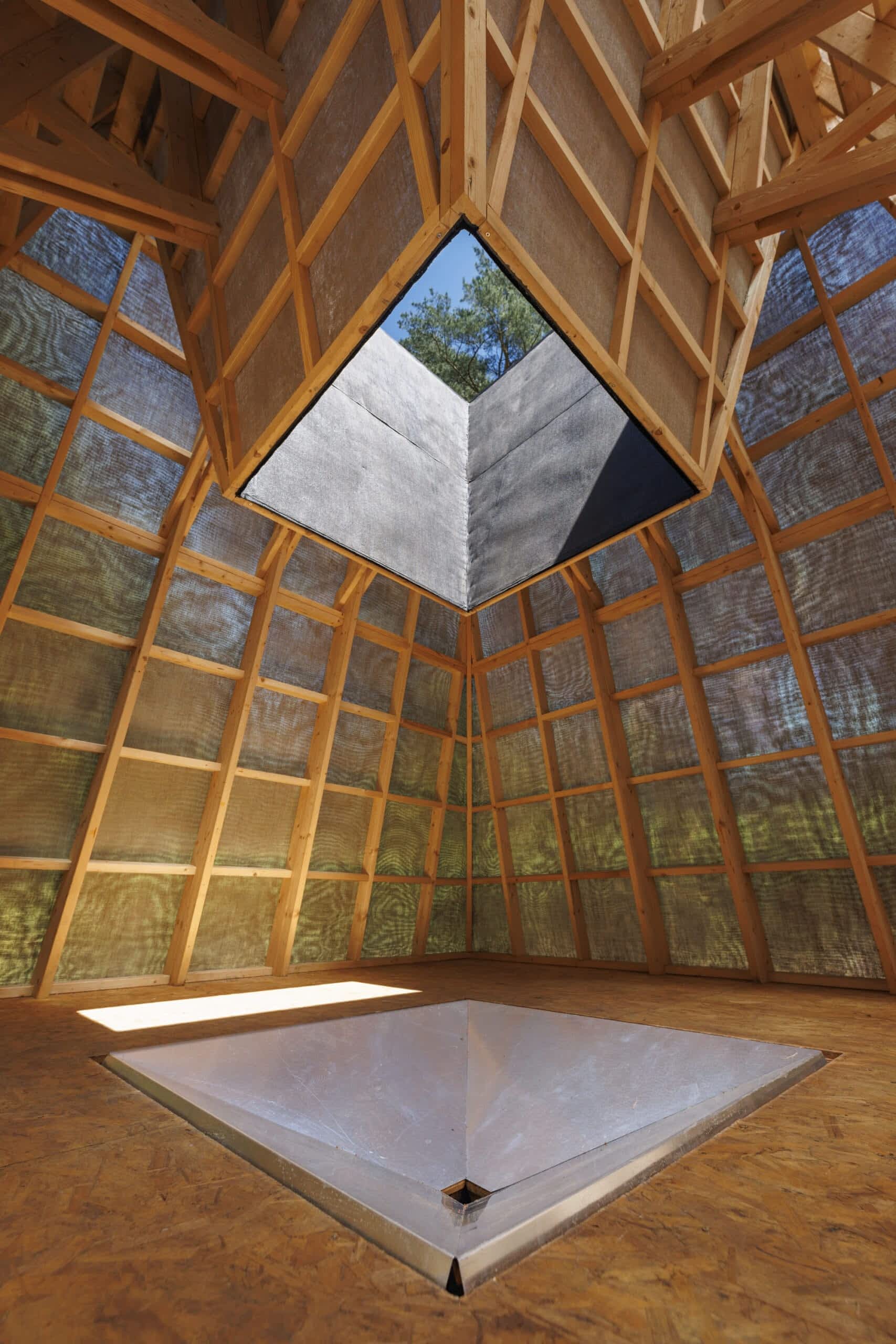 a detailed interior view of the previous geometric wooden building covered with black tarps. the inside retains a lot of natural light within its light wood structure.