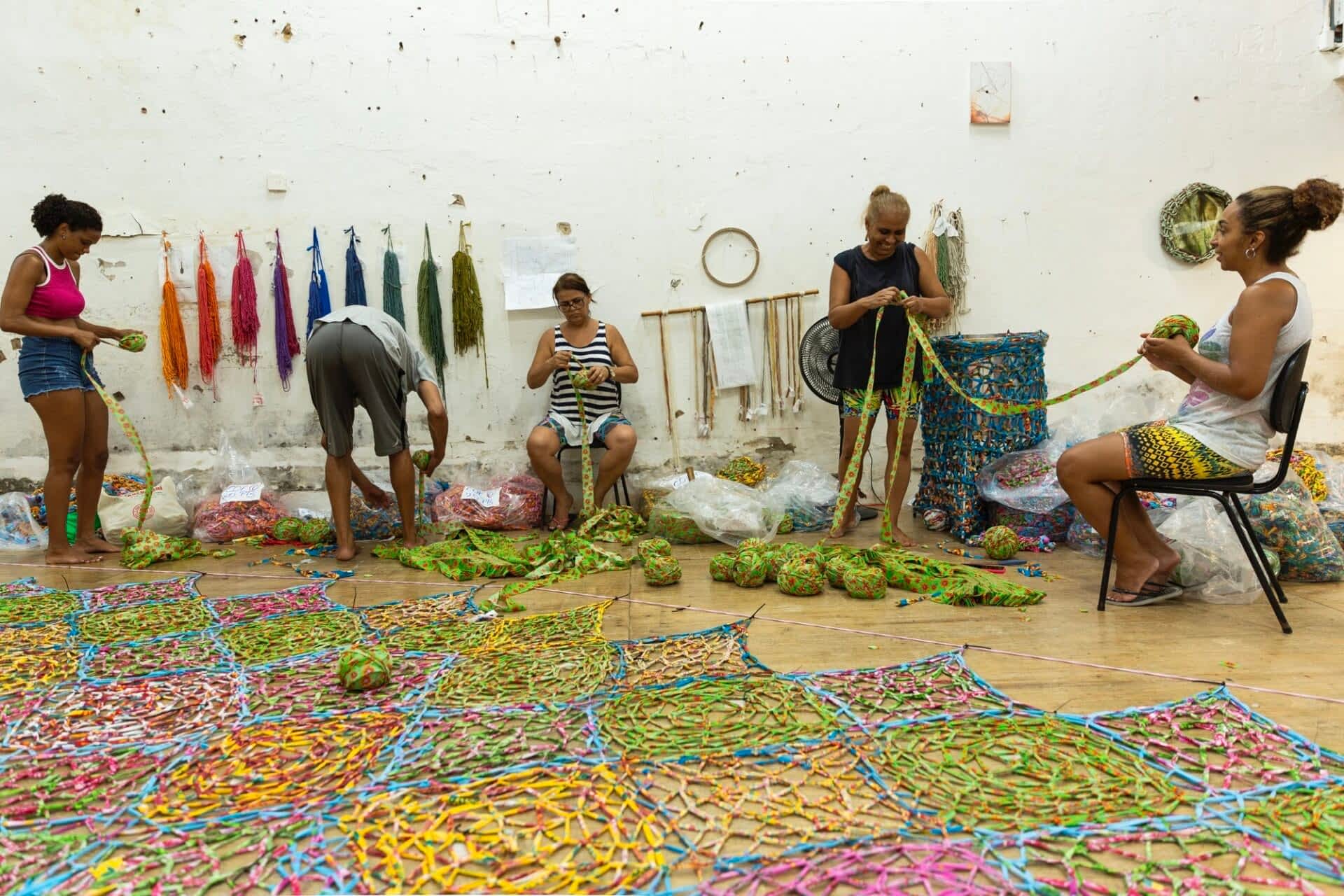 a group of assistants work on crocheting a large suspended sculpture made from strips of chintz fabric