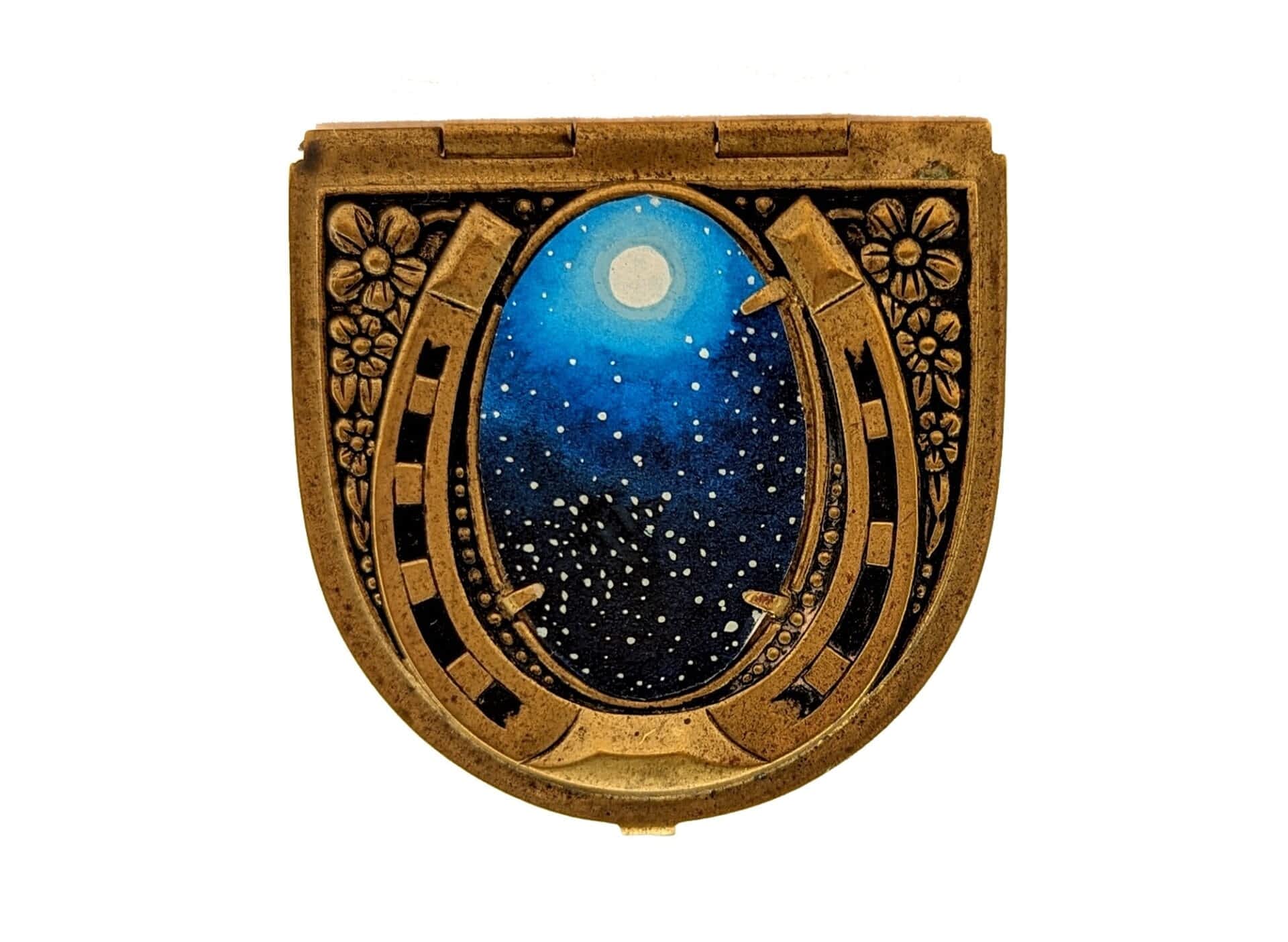 the exterior of a small, antique cosmetics compact with a starry scene applied to the front
