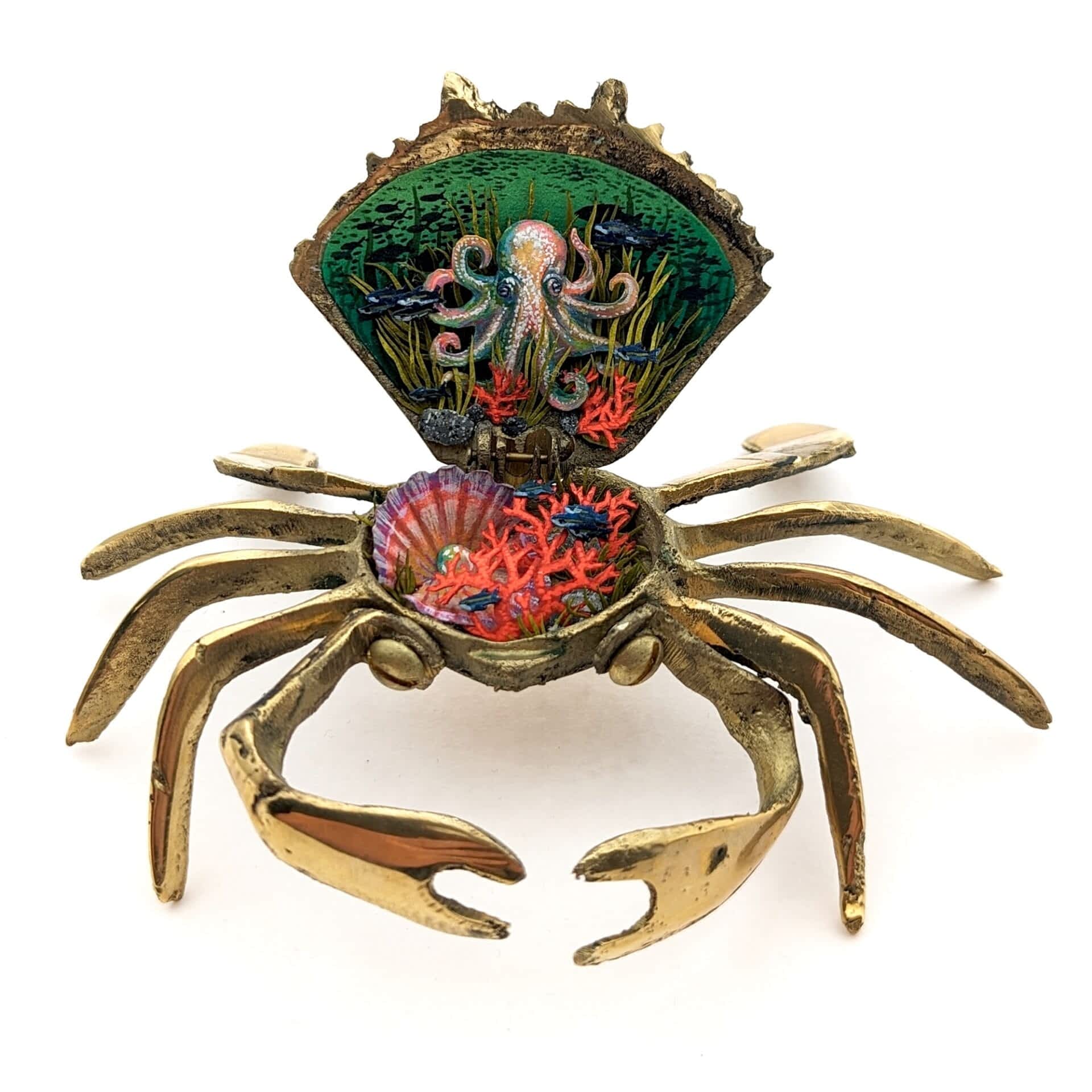 a tiny diorama made from watercolor-painted paper inside of a vintage brass crab-shaped compact depicting a sea scene with coral, shells, and an octopus