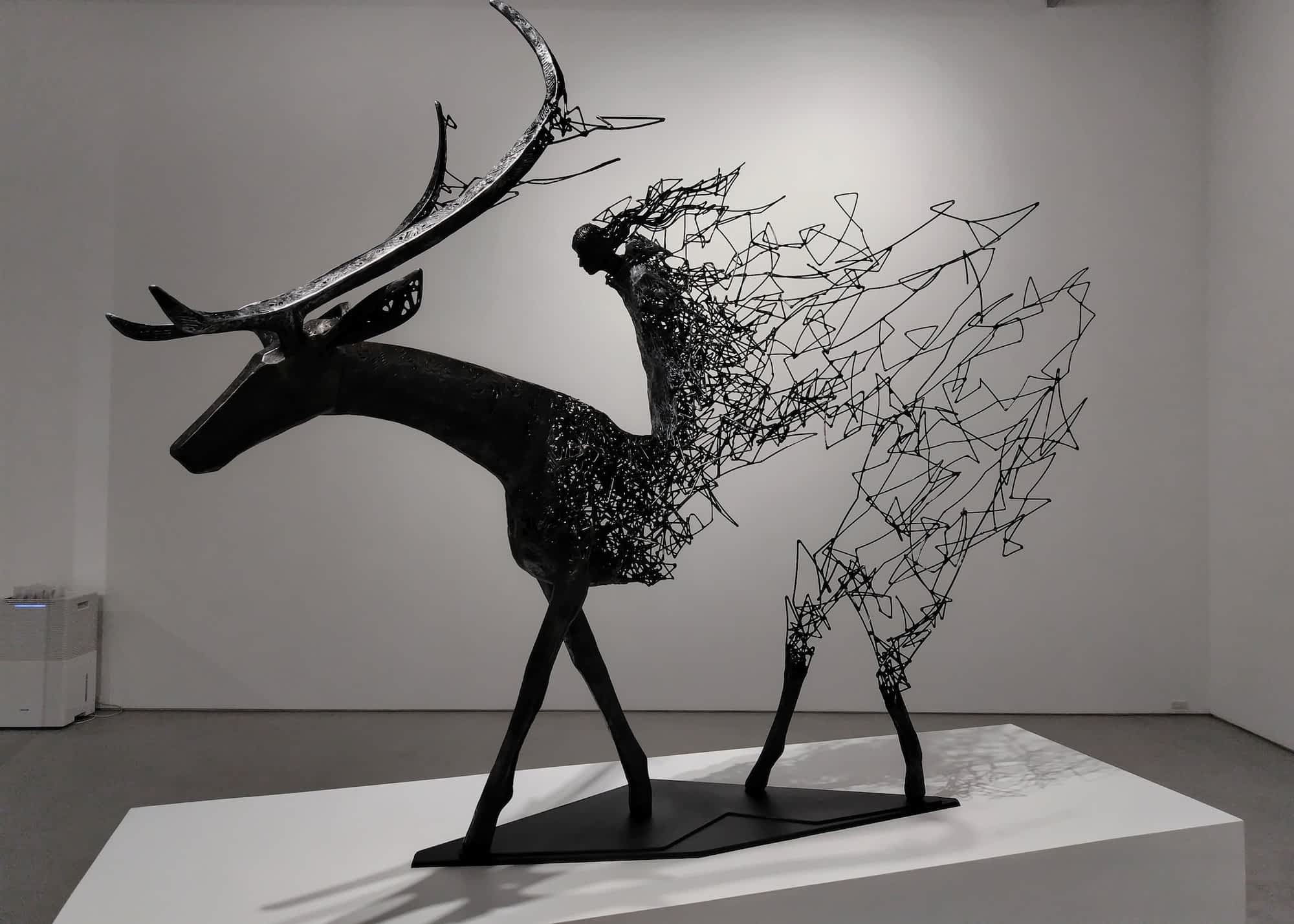 a metal abstract sculpture of a figure riding a giant deer with its center missing and tendrils leading toward the sky as if it is disintegrating upward