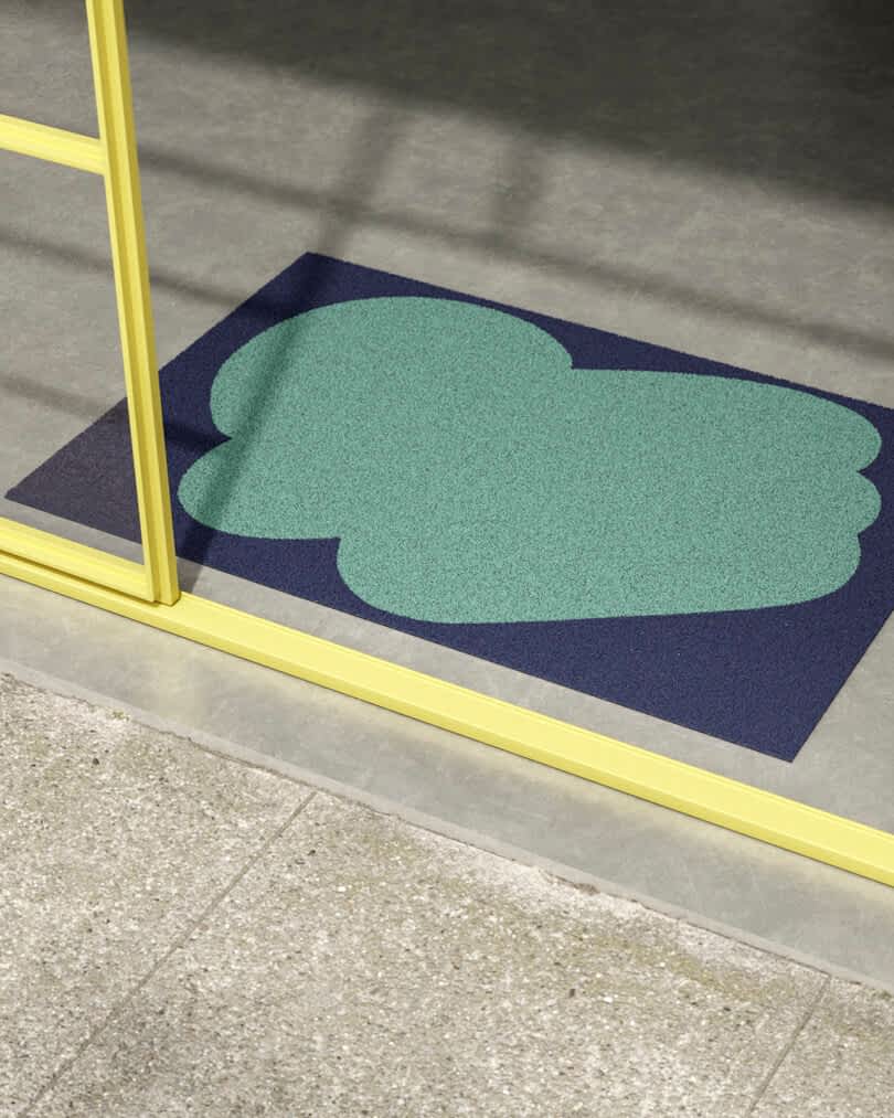 An abstract blue and green doormat placed on a concrete floor inside a building entrance with glass doors 