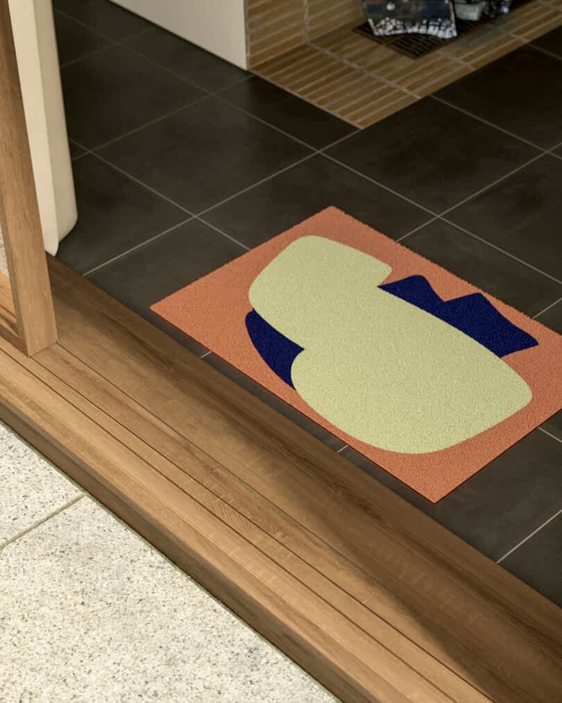 A colorful doormat with abstract design on a tiled floor by a wooden door threshold