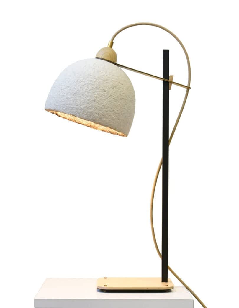 A modern table lamp from the MushLume Lighting collection, featuring a curved stem, black stand, and white dome-shaped shade, elegantly placed on a rectangular white base.