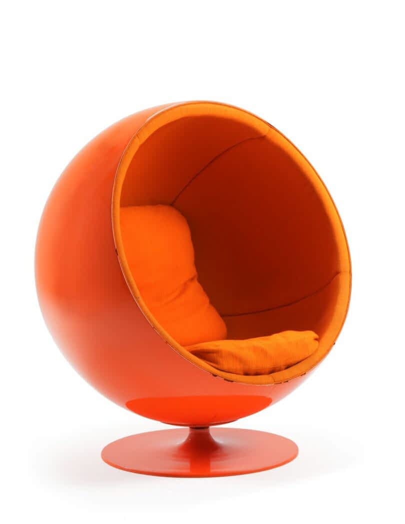 A modern, spherical orange chair with a cushioned interior and a swiveling base. The design resembles a partial globe with an open front