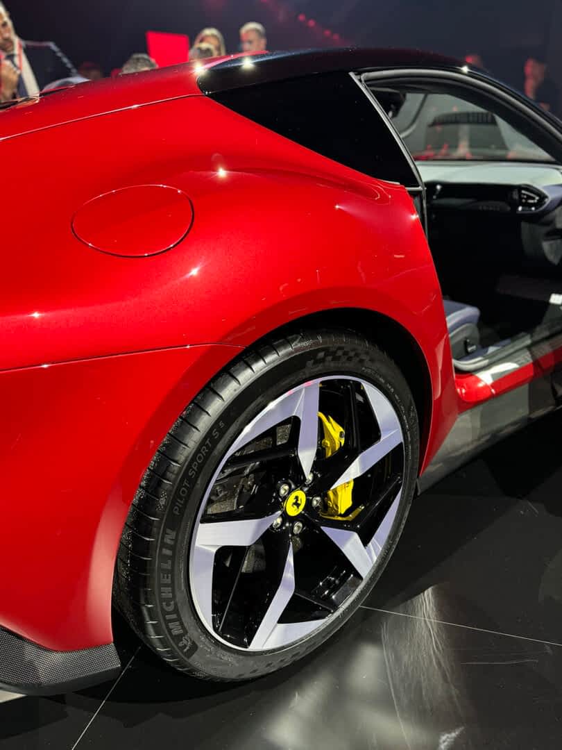Close-up view of a red sports car's rear quarter panel and wheel, featuring a yellow Ferrari logo on the brake caliper.