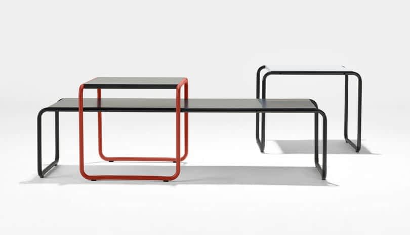Three modern nesting tables: a red-bordered table on top of a larger black table, next to a separate smaller black table, all with minimalist metal frames and flat surfaces.