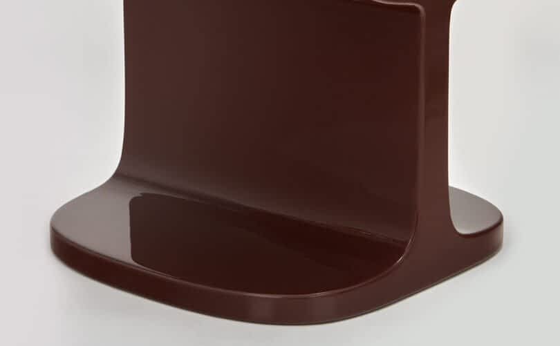 Close-up of the base of a brown modern chair against a neutral gray background.