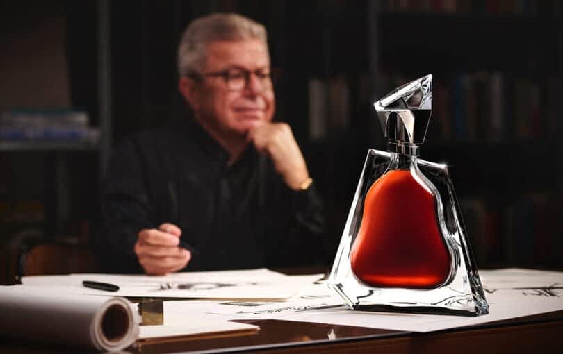 Architect Daniel Libeskind sitting at a desk with papers, with a Richard Hennessy Baccarat crystal decanter bottle filled with cognac is positioned prominently in the foreground.
