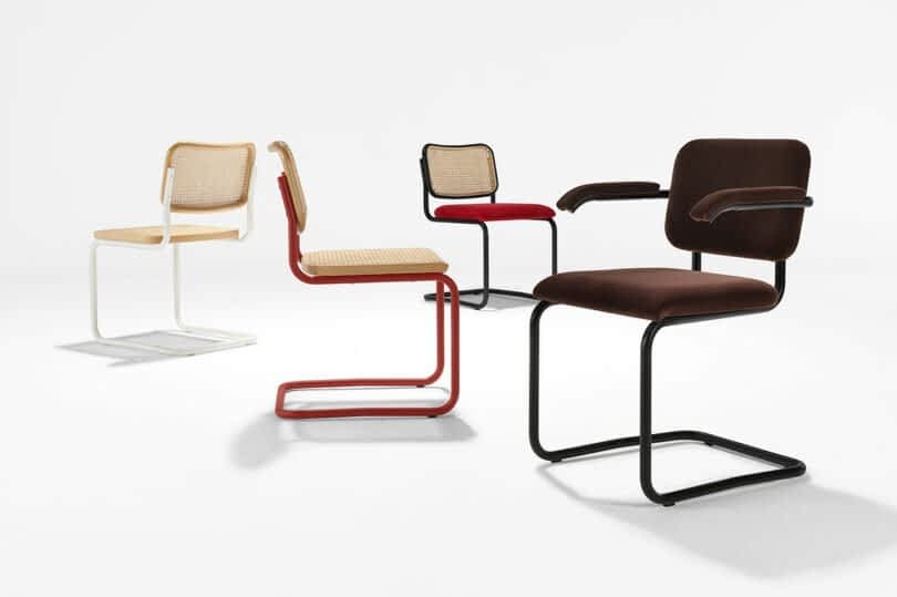 Four modern chairs in a white studio: two have cane seats and backs with metal frames, one in white and one in red; two have upholstered seats and backs with armrests, one in red and one in brown.