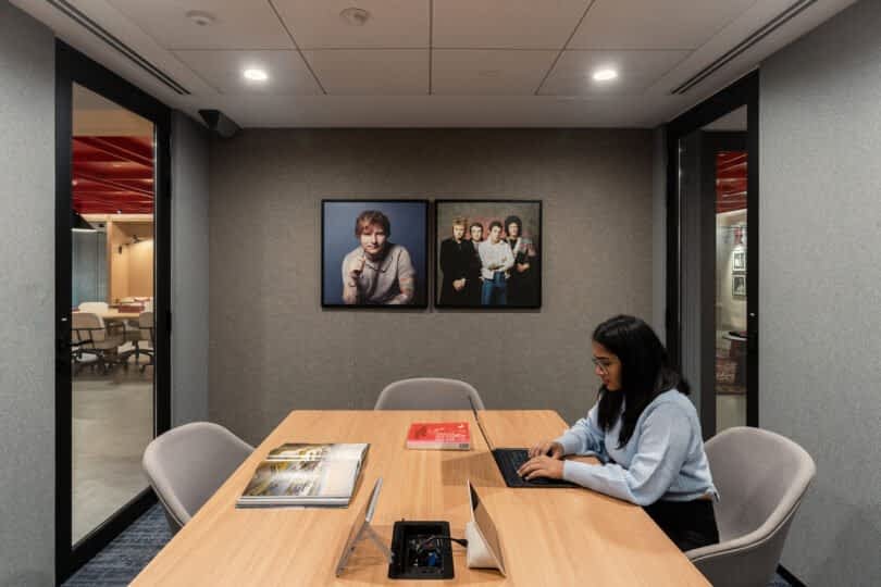 A woman works on a laptop at a conference table in a modern office meeting room with framed photos on the wall and various items on the table