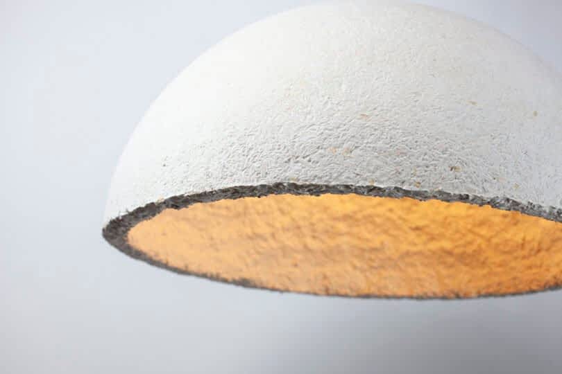 Close-up of a dome-shaped, textured white light fixture from MushLume Lighting, lit with a warm yellow glow and set against a plain white background.