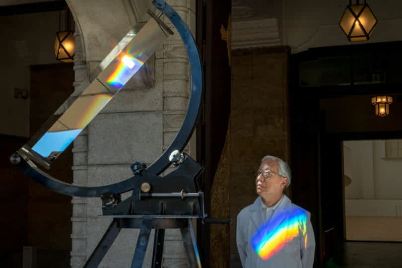 Artist Hiroshi Sugimoto with prism and rainbow across chest.