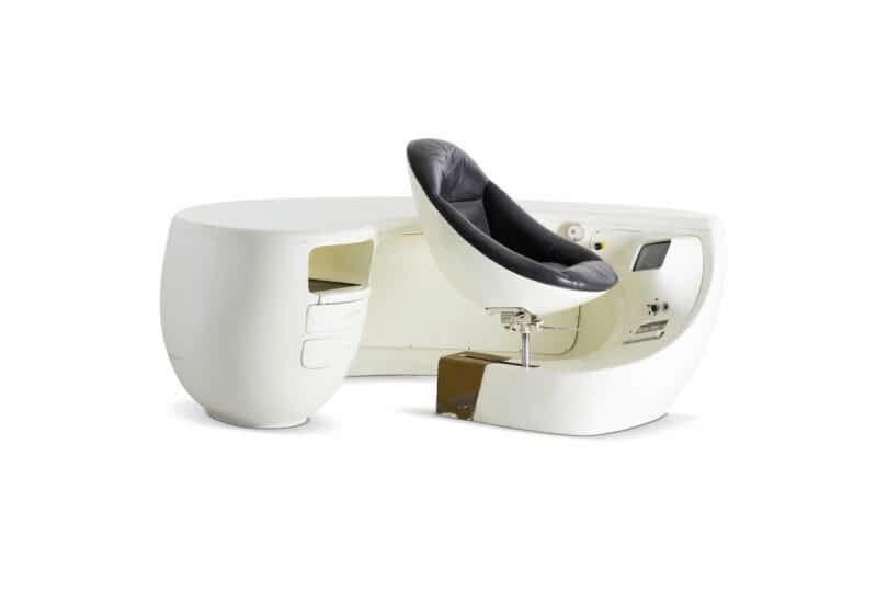 A white pod-shaped desk with an integrated black chair, featuring a built-in control panel and storage compartments