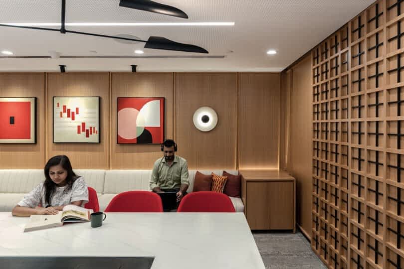 Two people, one reading a book and the other using a tablet, sit in a modern room with abstract art on the walls and a geometric wooden partition