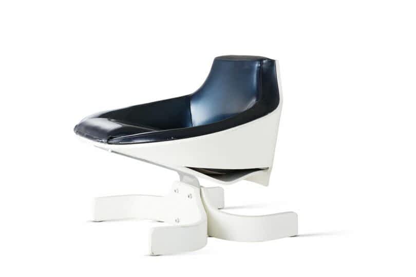 A white modern chair with a sleek, curved design and a dark blue cushioned seat. The chair features a unique, cantilevered base on a white stand
