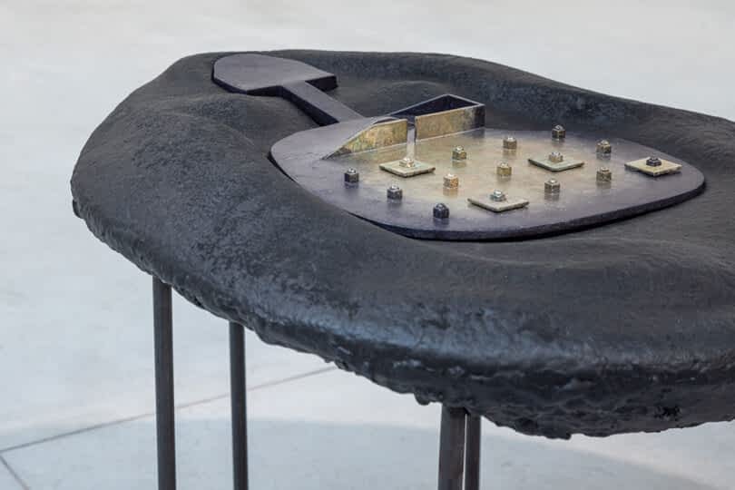 Modern abstract sculpture with an irregular black surface and industrial elements, including bolts and metallic structures.