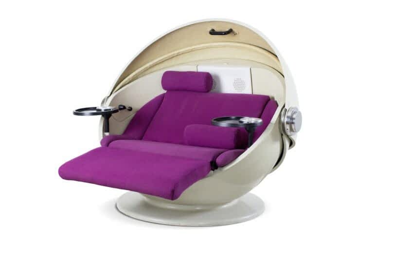 A unique white spherical chair with purple cushioning and built-in trays attached to the sides. The chair has a padded headrest and armrests