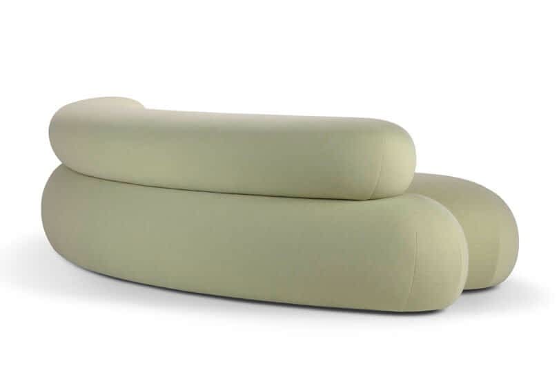 A light green modern sofa with smooth, rounded curves and a minimalist design, photographed from the back.