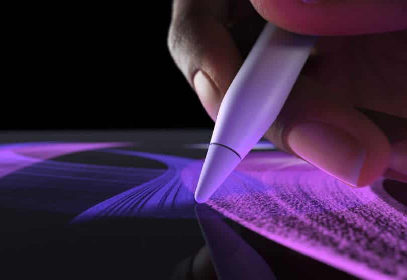 Close-up of a hand using the Apple Pencil Pro drawing purple lines on an Apple iPad Pro's digital tablet screen.