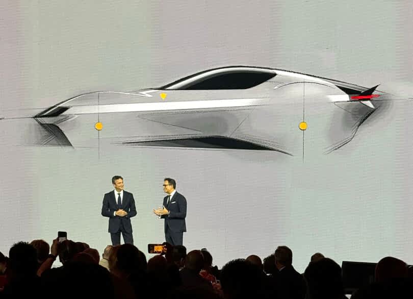 Two men in suits presenting a Ferrari 12Cilindri sports car design on a large screen at an automotive event.
