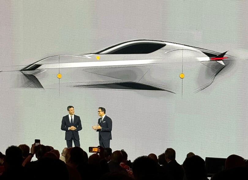 Two men in suits presenting a Ferrari 12Cilindri sports car design on a large screen at an automotive event.