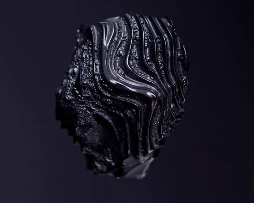 Close-up of a black object with intricate, wavy patterns on a dark background.