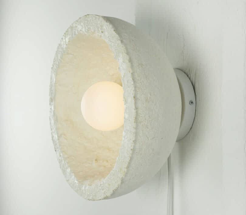 Close-up of a MushLume Lighting wall-mounted fixture with a textured, semi-spherical white shade and an exposed bulb in the center.