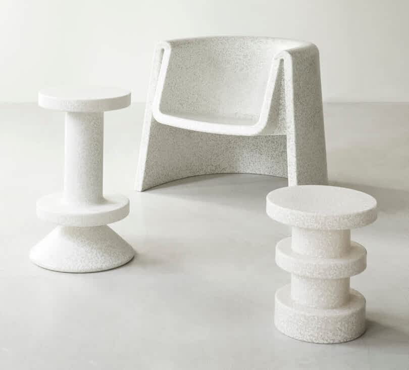 A white, speckled armchair is flanked by two matching, uniquely shaped side tables on a plain, light-colored floor.