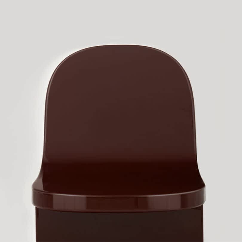 Close-up of the top of a brown modern chair against a neutral gray background.