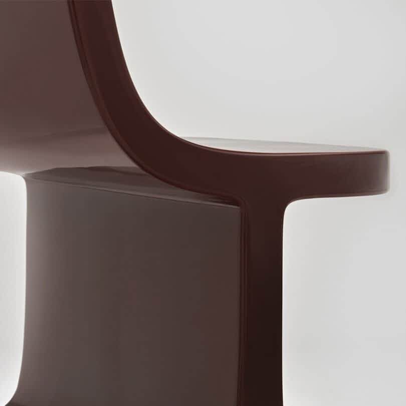 Close-up of a brown modern chair against a neutral gray background.