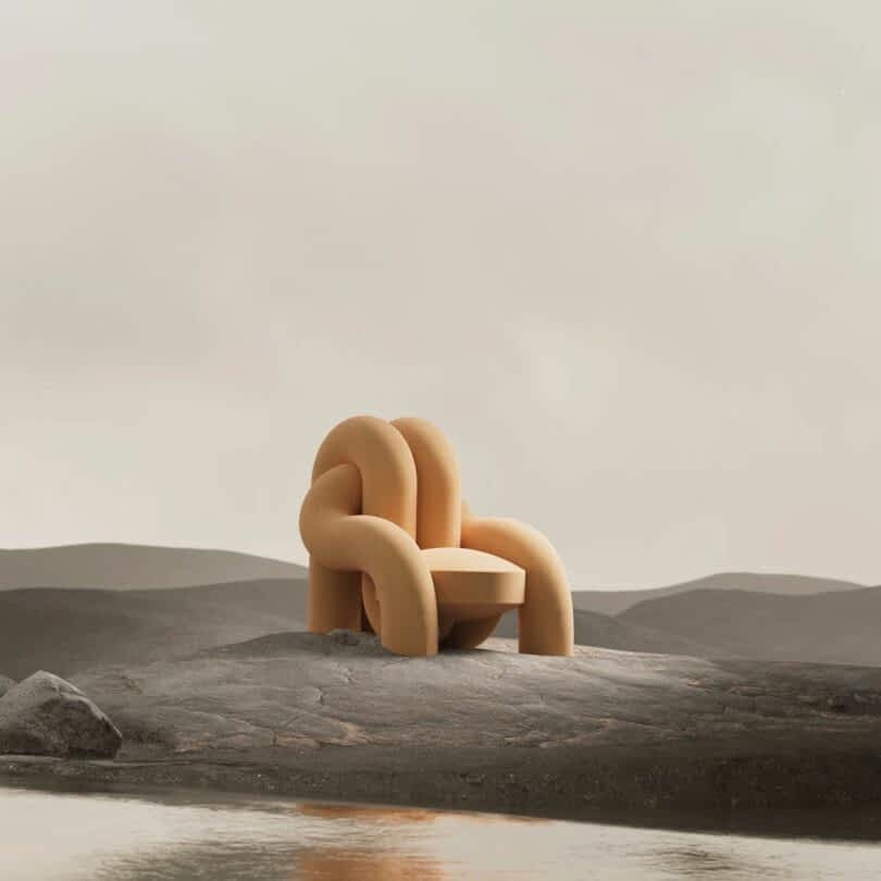 A uniquely designed, plush armchair with intertwined curves sits on a rocky, barren landscape by a calm body of water. The sky is overcast