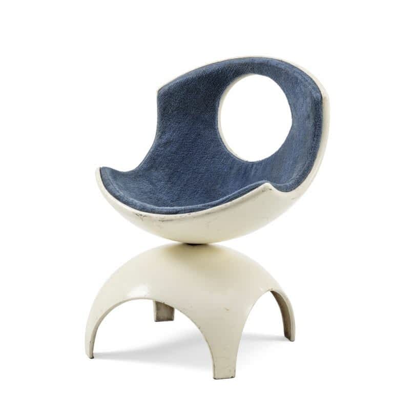 A modern chair featuring a white circular base and a curved seat with blue upholstery and a large circular cutout in the backrest
