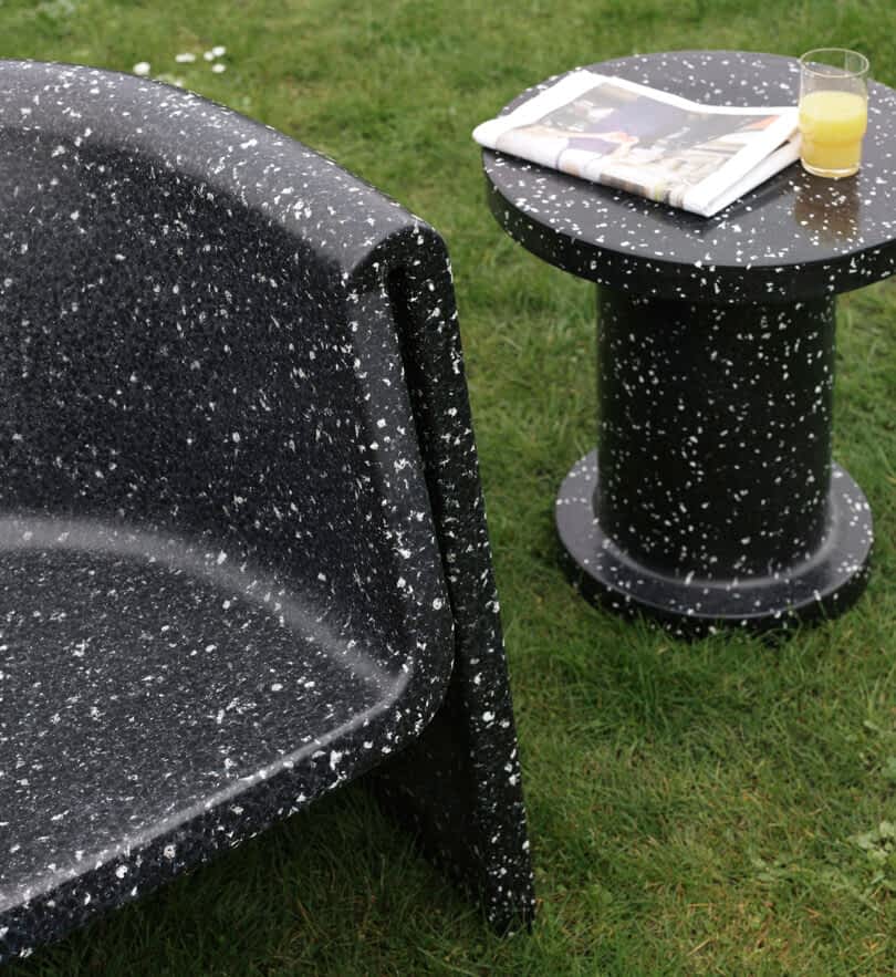 Outdoor lounge chair and a side table. The table has a newspaper and a glass of orange juice on it, placed on a grassy lawn.
