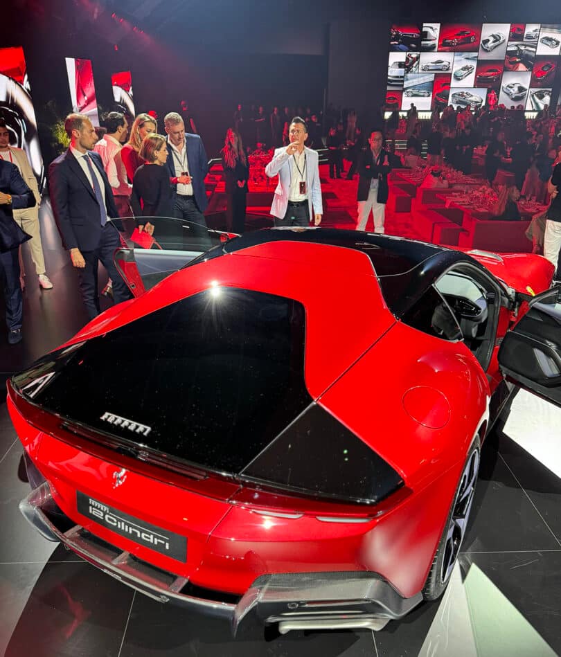 A Ferrari 12Cilindri sports car displayed at an exhibition with a crowd of people and presenters around it.