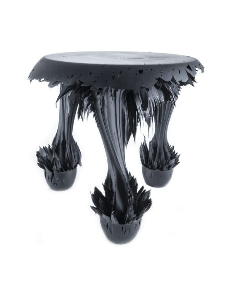 A sculptural table with a round top and three legs, appearing to be made from a dark, glossy material that has a melting or stretching texture