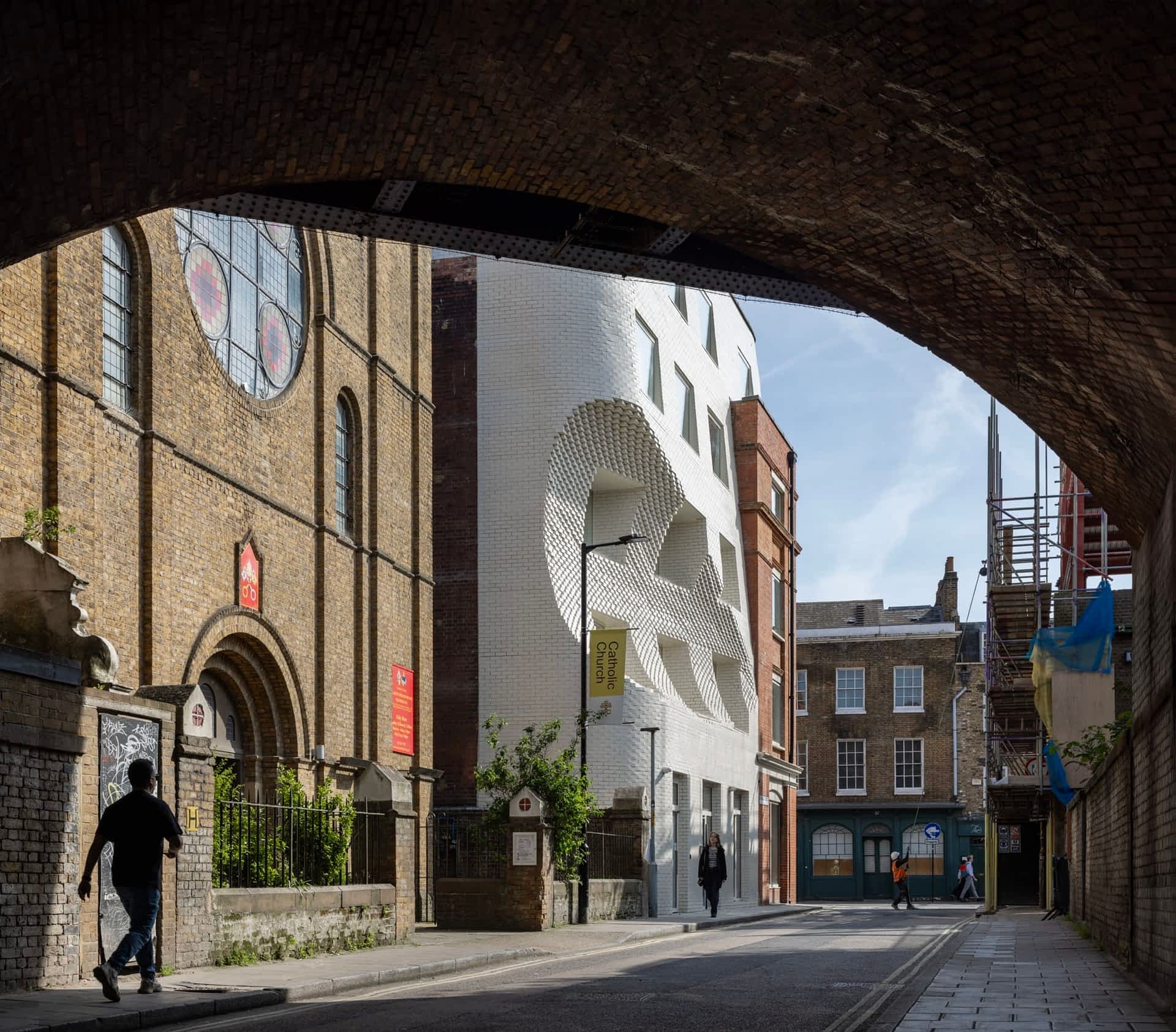 a building in London viewed from beneath a bridge, showing people walking along the street in front of a white brick building with a large scoop shape in the facade