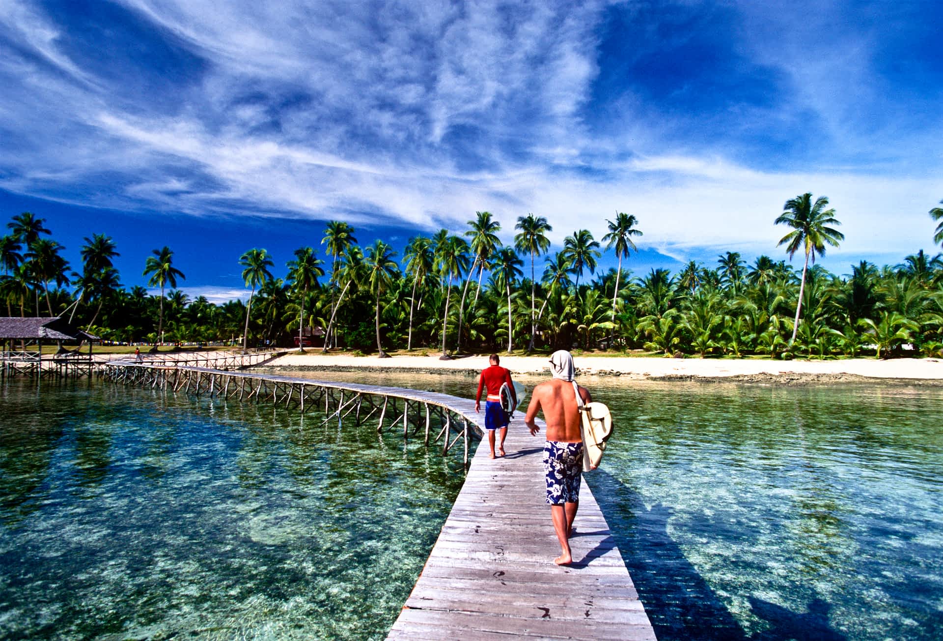 Surfers walk along a billboard in front of a sandy beach on Siargao Island. Surfers walk along a boardwalk on Siargao Island, The Philippines