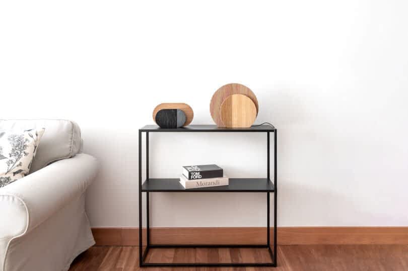 A black metal console table with books and wooden lamps is placed against a white wall, next to a light gray sofa.