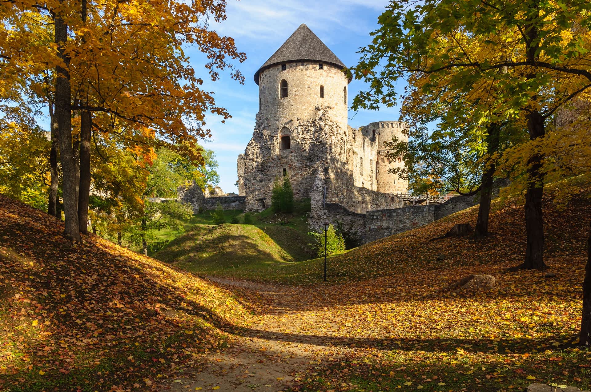 Latvia castle Medieval castle ruins sit in a forest where leaves are turning yellow in fall.