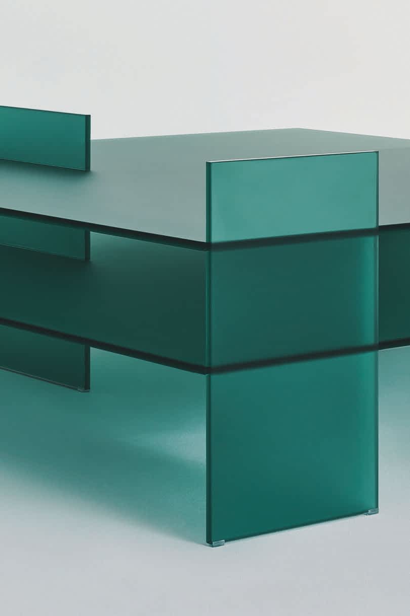Detail of a minimalist green glass table displayed against a plain background.