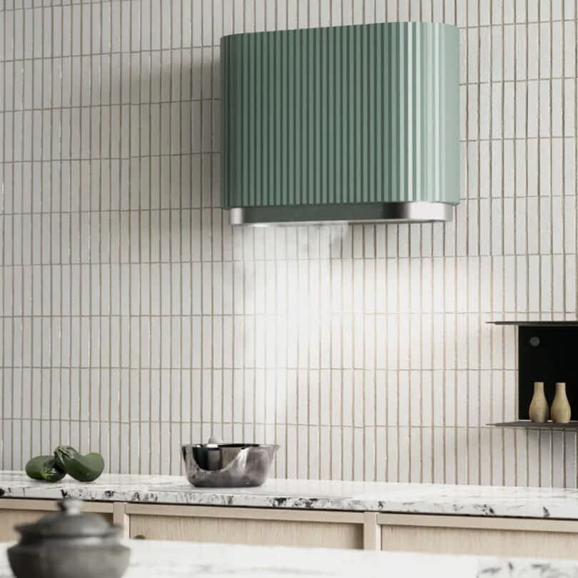 Modern kitchen with a Ciarko Design Mono kitchen hood mounted on a tiled wall above a white countertop, with decorative bowls and vases, sucking in steam from a bowling pot below.