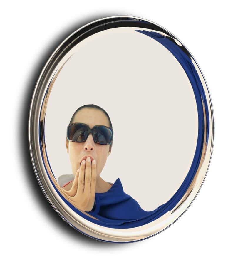 A woman ins reflected in a round mirror with a metallic frame.