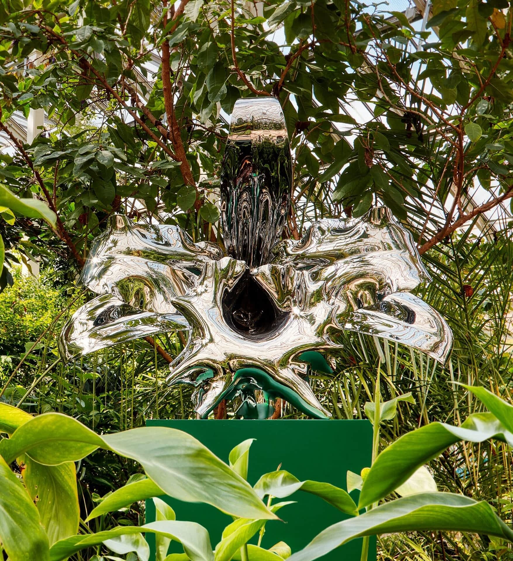 a larger-than-life sculpture of an orchid inside a greenhouse, surrounded by tropical plants