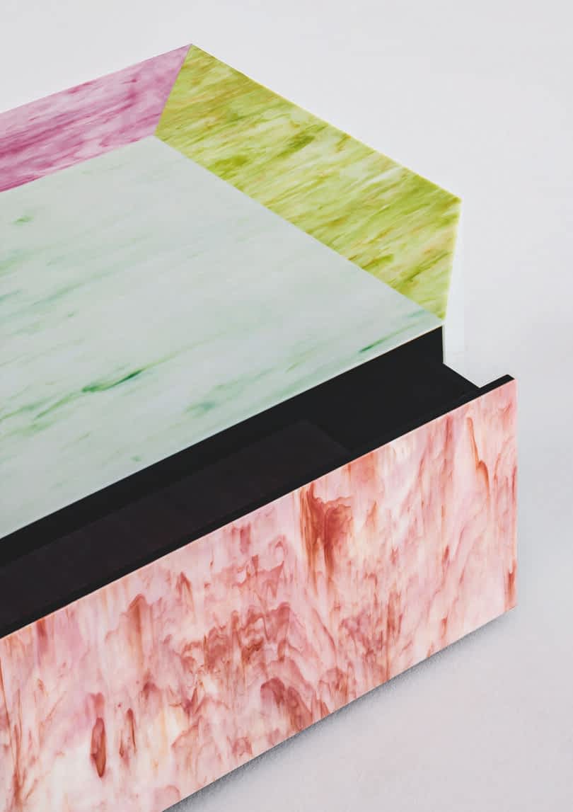 Detail of a multicolored geometric coffee table featuring shades of pink, green, and purple with a marbled texture on a plain background.