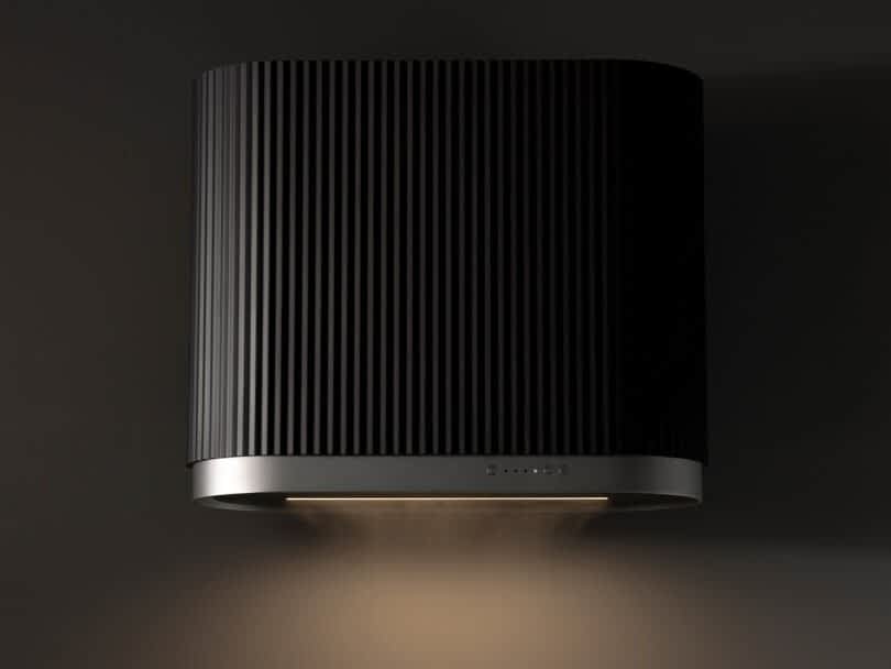 A modern cylindrical black Ciarko Design wall mounted kitchen hood emitting soft light downwards, positioned against a dark gray background.