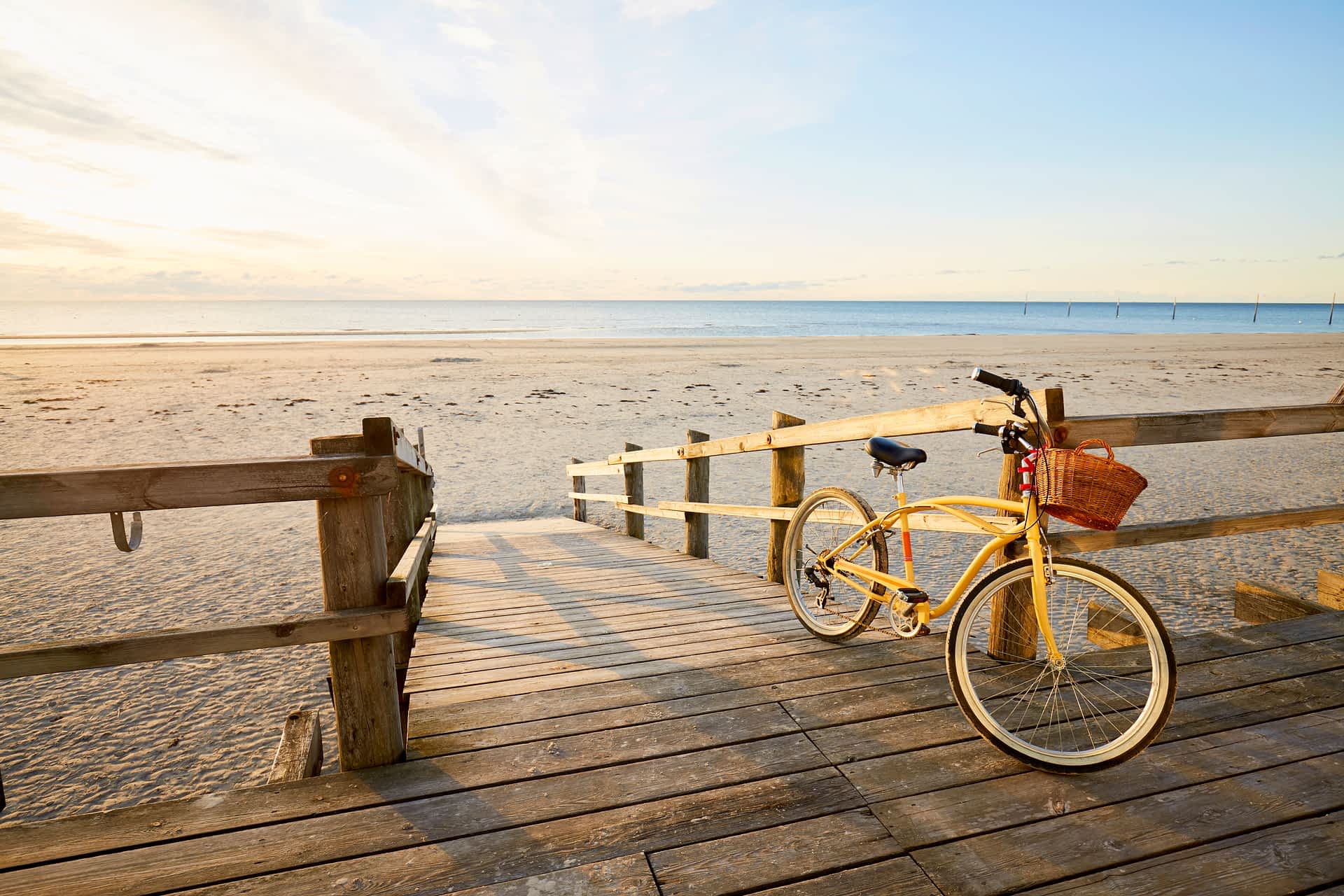 GettyImages-1193733541.jpg A yellow bicycle leans against wooden railings at the top of a sandy beach as the sun rises