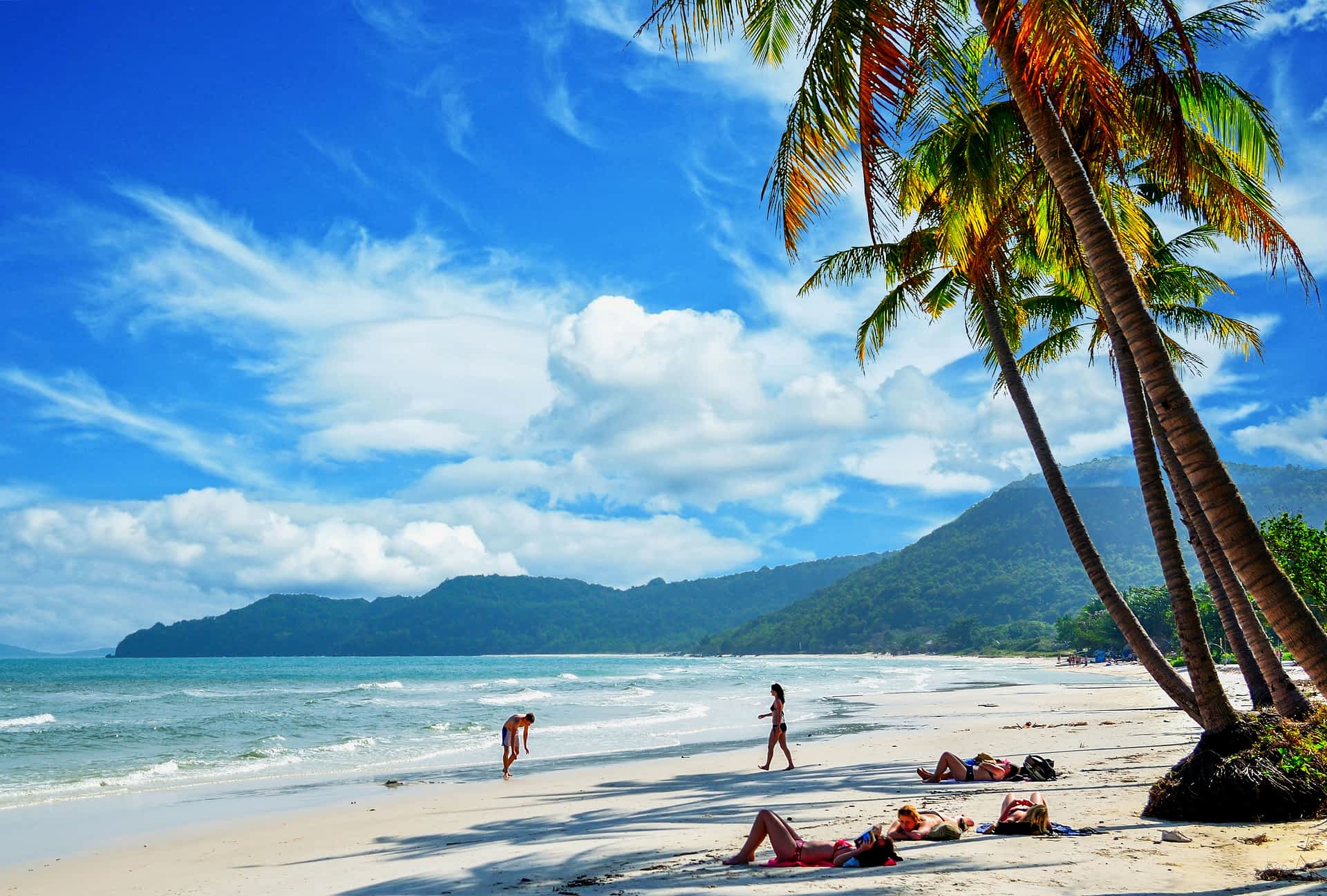 People lay on a white sand beach under palm trees on Khem Beach, Phu Quoc