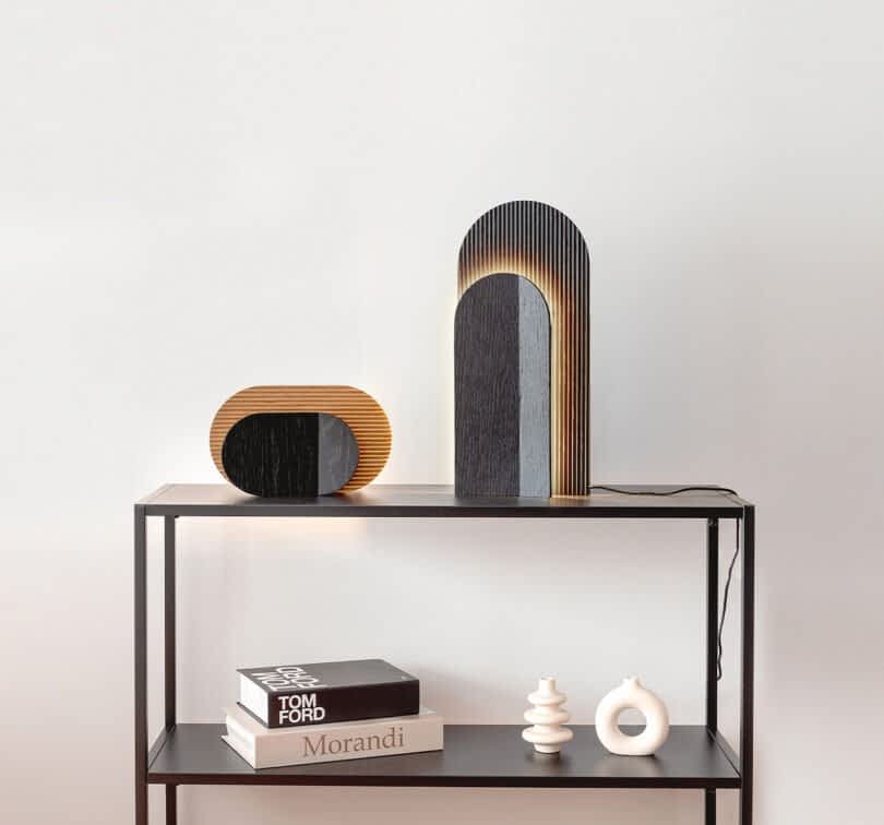 A minimalist metal shelf showcasing art pieces, books, and two wooden lamps